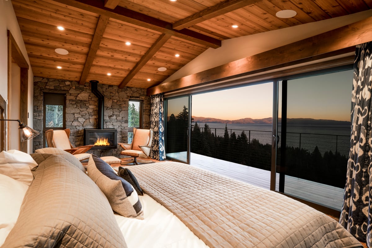 Interior bedroom with wood beams, stone fireplace, and lake sunset view