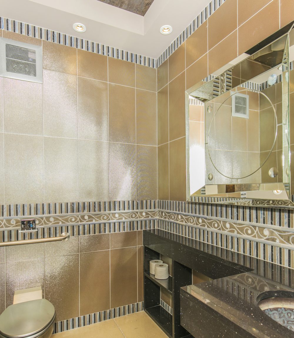 Bathroom with tan tiled walls, a large geometric mirror, and dark stone vanity.