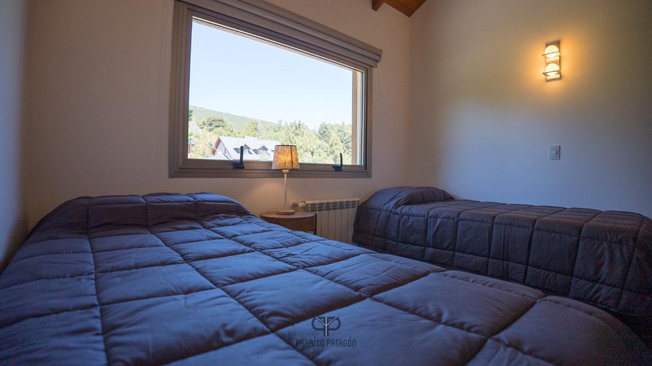 Bedroom with two dark blue quilted beds and a large window overlooking wooded hills.