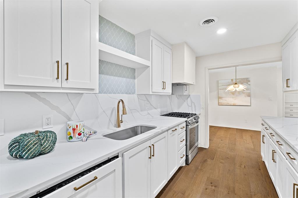 Renovated white kitchen with marble-look surfaces, brass fixtures, stainless steel range, and warm wood flooring.