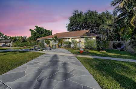 Single-story home at dusk beyond a curved stone walkway, with lit windows and mature palms.