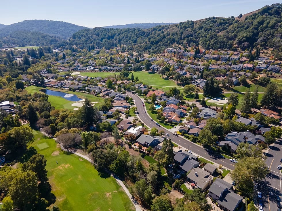 Aerial view of homes and a golf course nestled in a green, wooded valley.