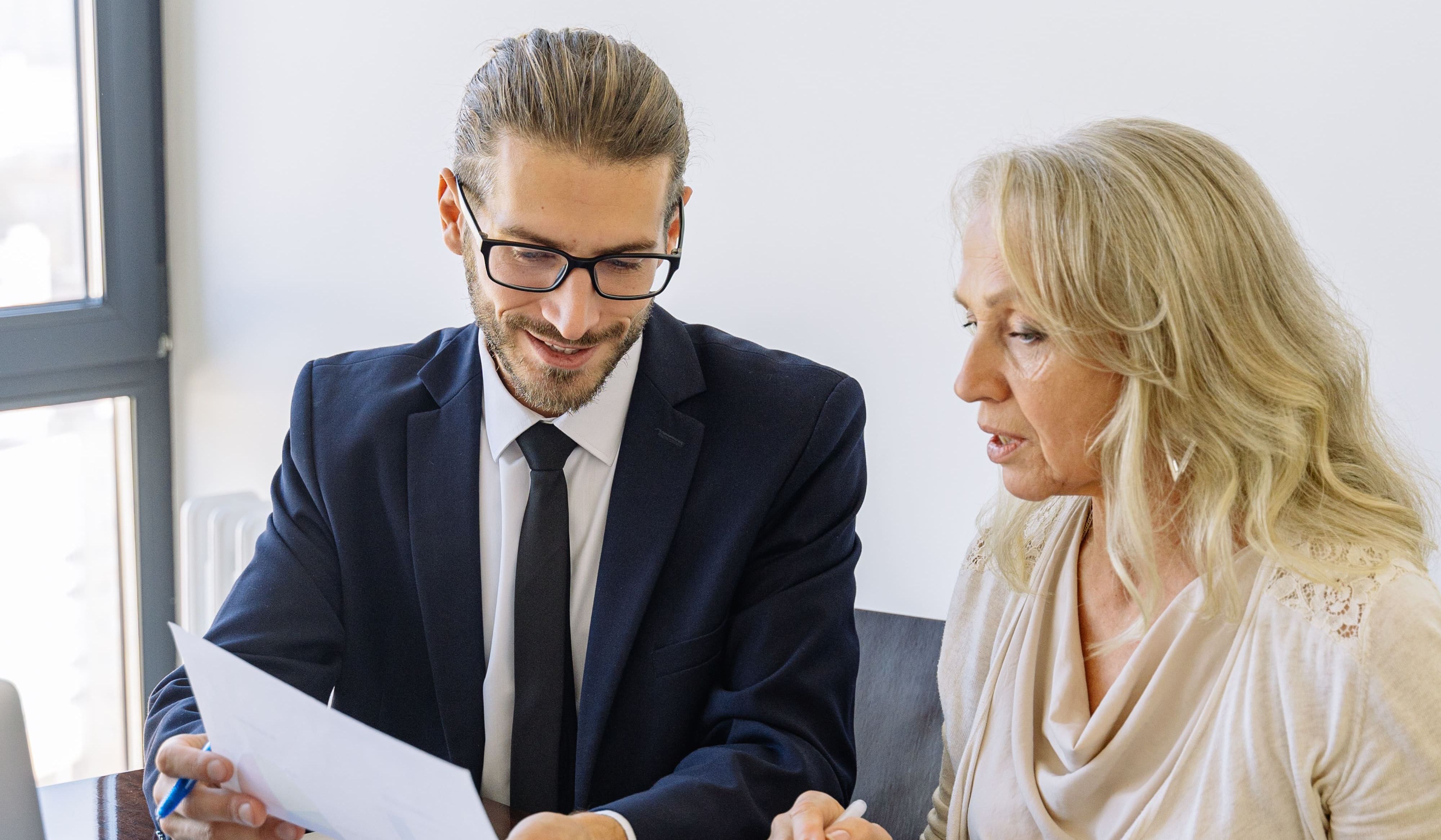 Real estate agent and woman reviewing paperwork together at a table.