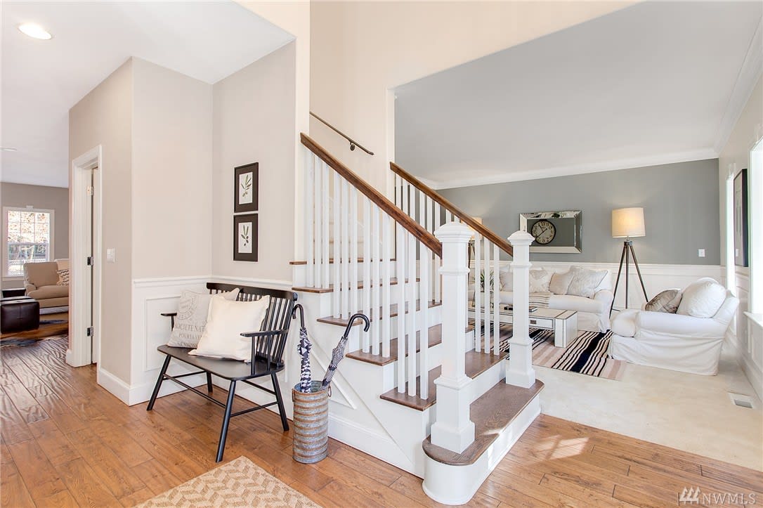 Furnished entry and living room with a white staircase, wood treads, and white seating.