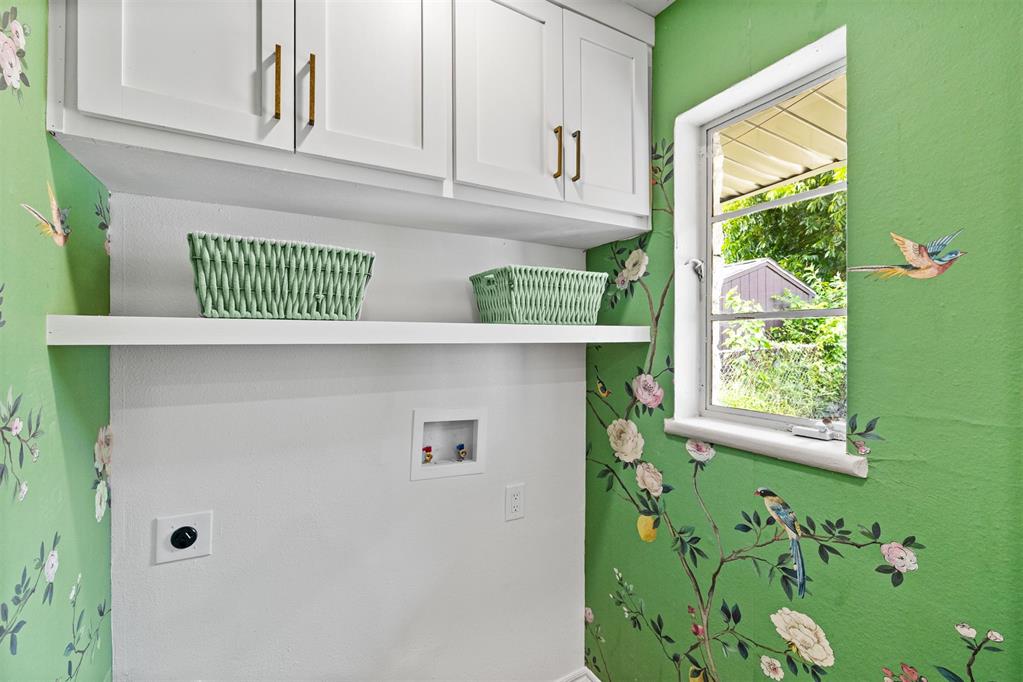 Laundry area with white cabinets, woven baskets, and green floral wallpaper beside a window.