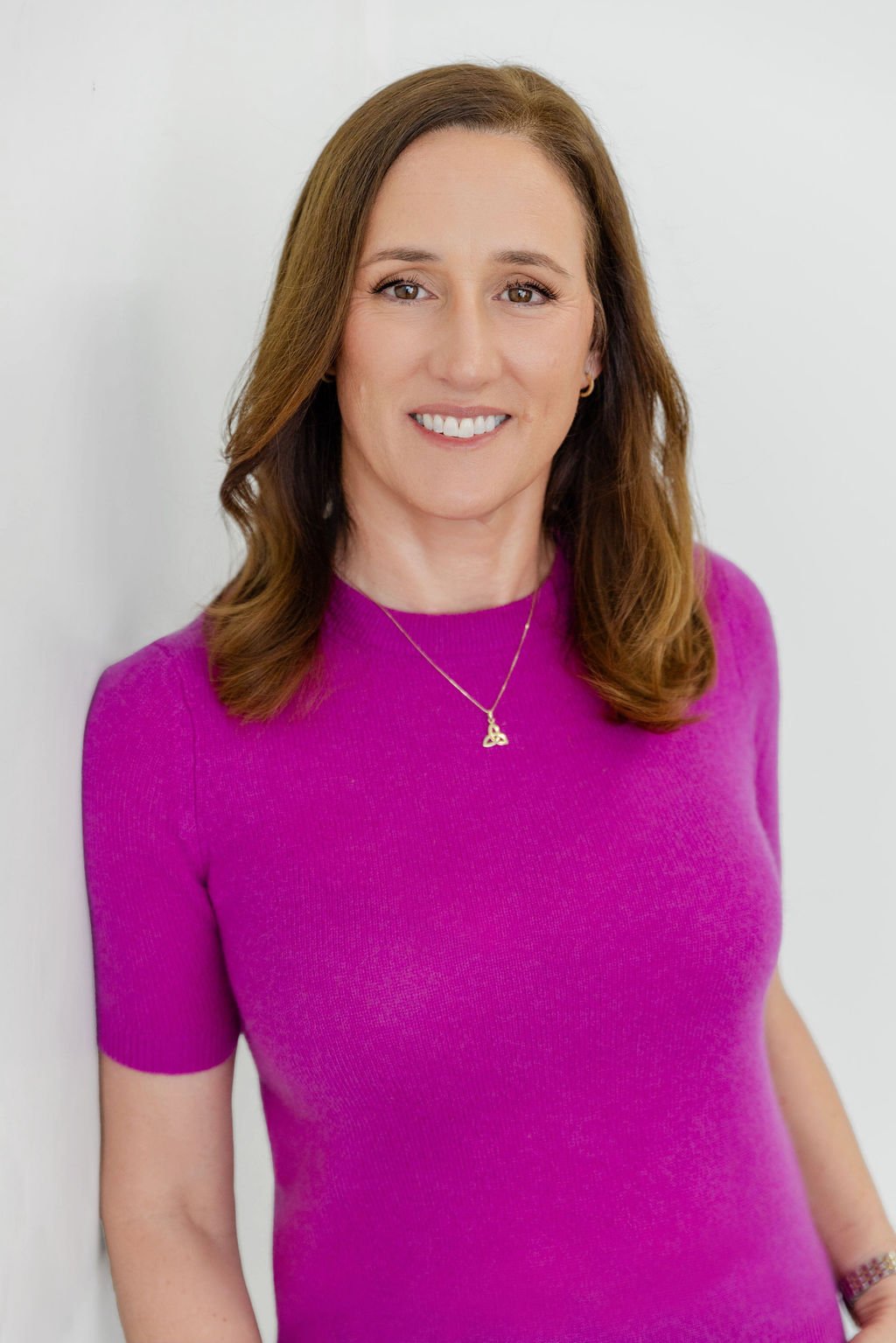 Anna Doherty Rivas smiling in a magenta top and pendant.