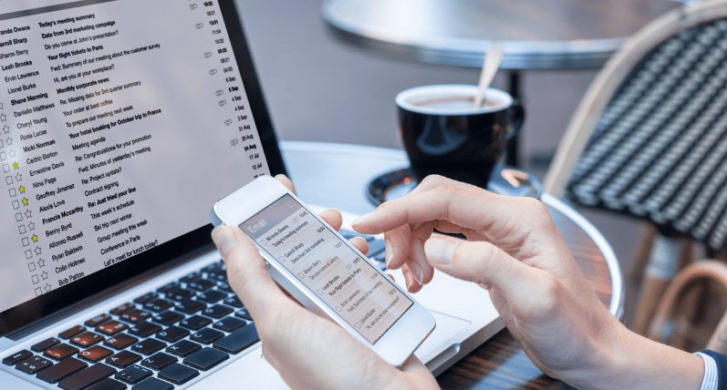 Hands using a smartphone beside an open laptop and coffee cup.