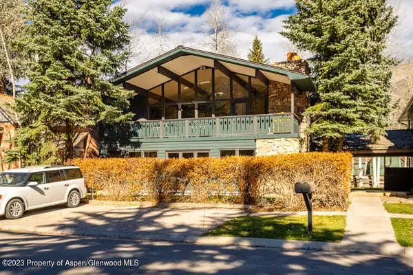 Mountain home with a glass gable, stone walls, green balcony, and golden hedge.
