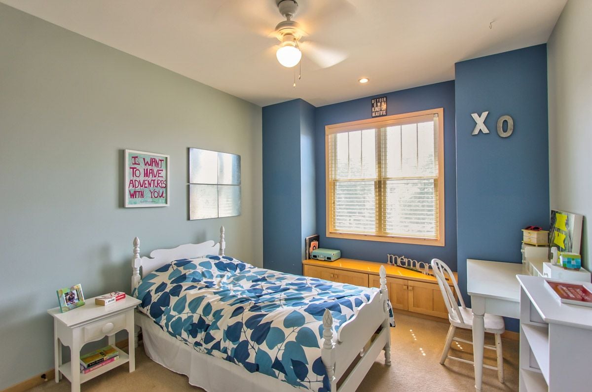 Bedroom with blue-and-white bedding, a blue accent wall, and a sunlit window.