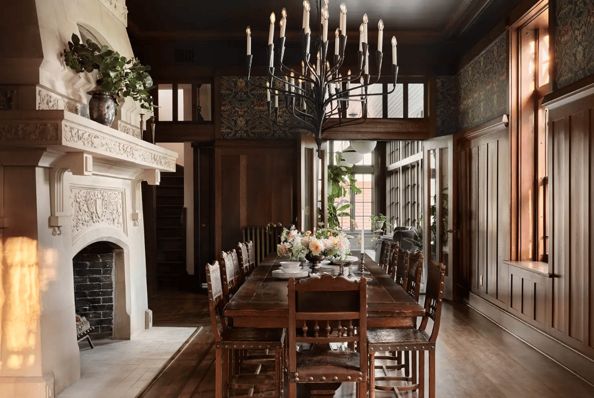 Dining room with a long dark wood table, ornate white fireplace, and tall chandelier.