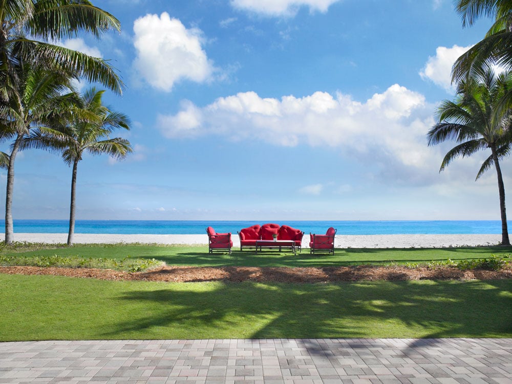 Oceanfront lawn with red lounge seating, palm trees, and a sandy beach.