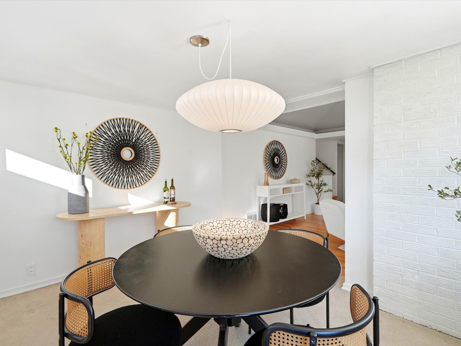 Dining room with a round black table, cane-back chairs, and a large pendant light.