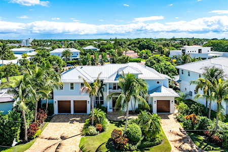 Modern East Boca home with a white roof, palm trees, and tropical landscaping.