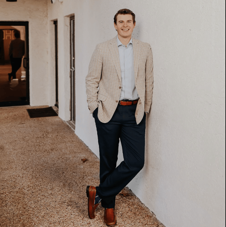 Daniel Donaldson in a checked blazer, standing against a white stucco wall.