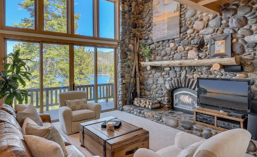 Lakefront living room with tall windows and a rounded-stone fireplace wall.
