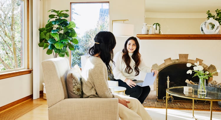 An image of two women conversing in a well-decorated living room, likely discussing real estate or home buying/selling topics.