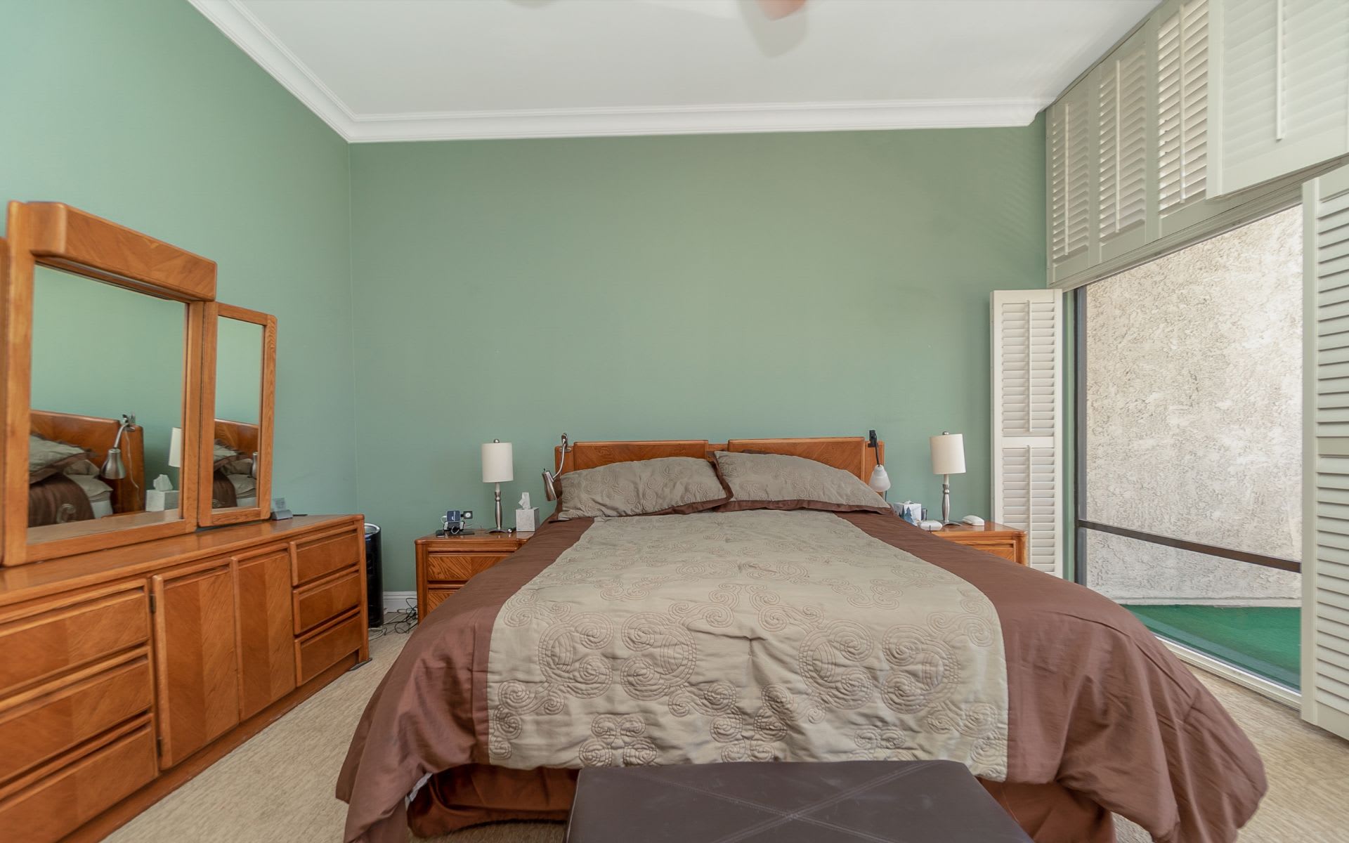 Bedroom with a large bed, matching wooden dresser and mirror, and a shuttered sliding glass door.