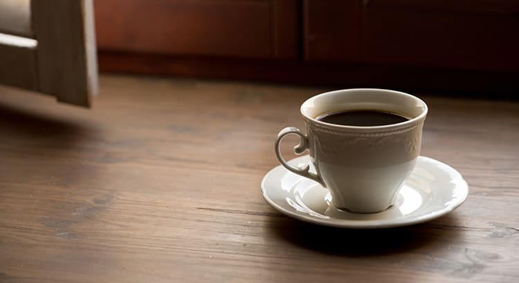 A close-up of a cup of coffee on a saucer, placed on a wooden surface, symbolizing relaxation, home life, or a morning routine.