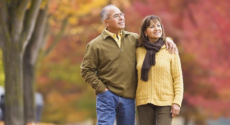 The older man and woman are dressed warmly, walking side by side, and enjoying a serene autumnal setting.