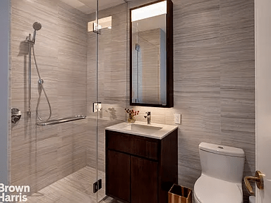 Bathroom with gray stone tile, glass-enclosed shower, dark wood vanity, and white toilet.