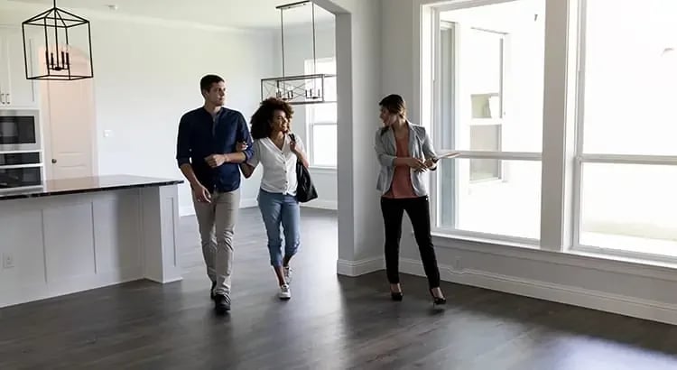 A couple walking through an empty house with a real estate agent, indicating a home tour or inspection.