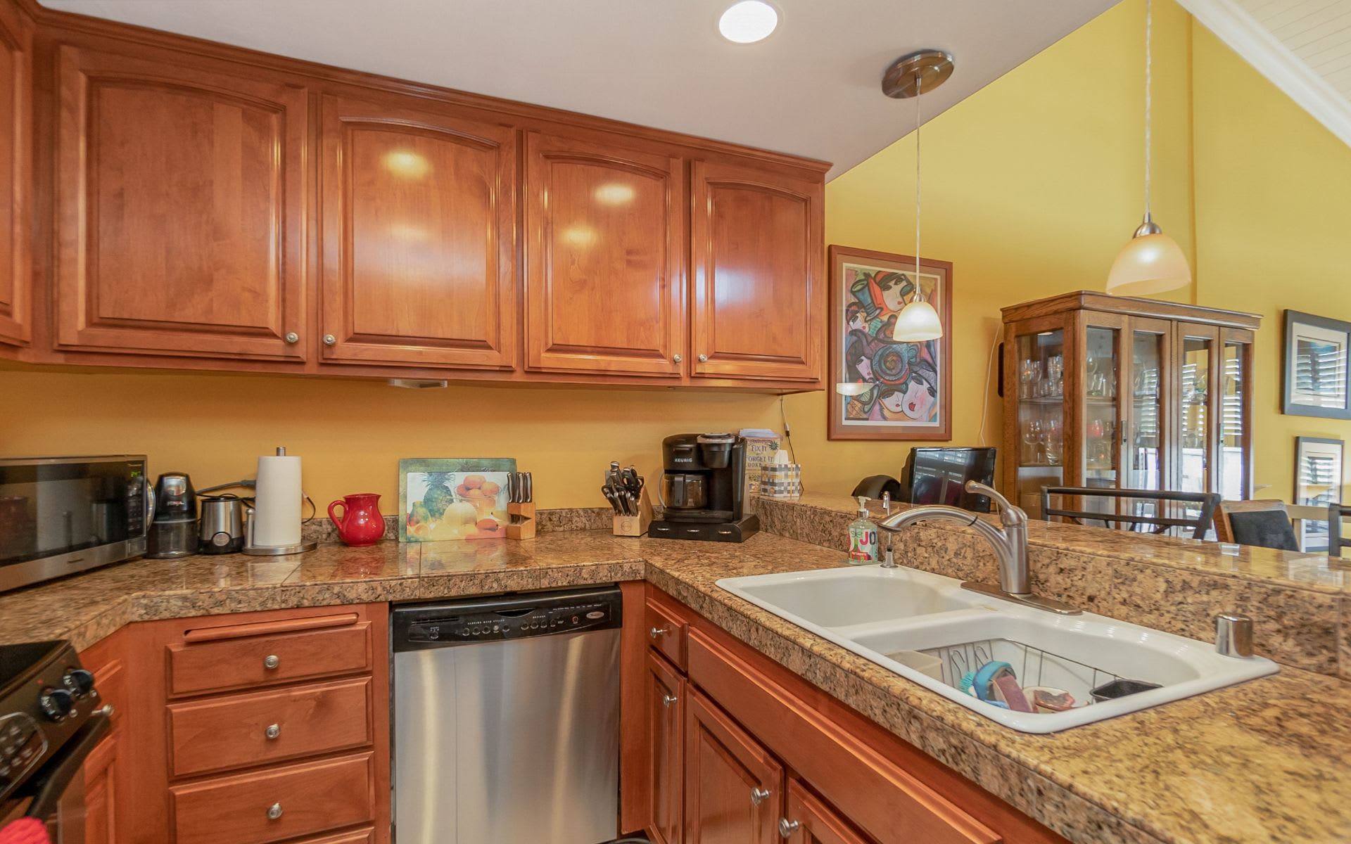 Kitchen with reddish wood cabinets, stone counters, a double-basin sink, and adjoining dining area.