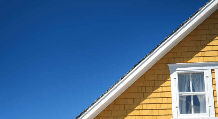 The upper section of a house with a steeply pitched roof and yellow wooden exterior wall.