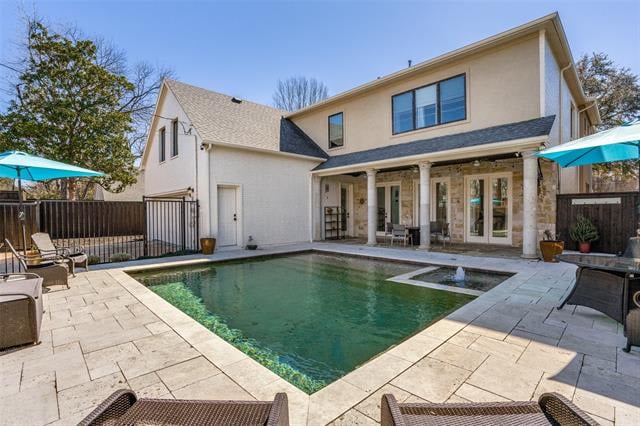 Two-story home behind a rectangular pool, with a stone patio and turquoise umbrellas.