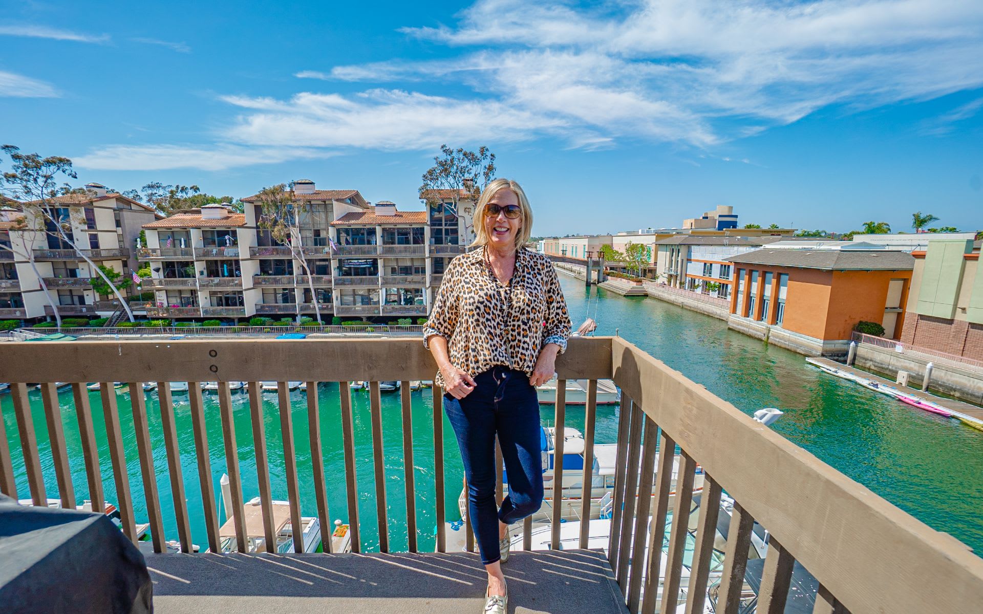 A woman on a waterfront balcony overlooking a canal and nearby condominiums.