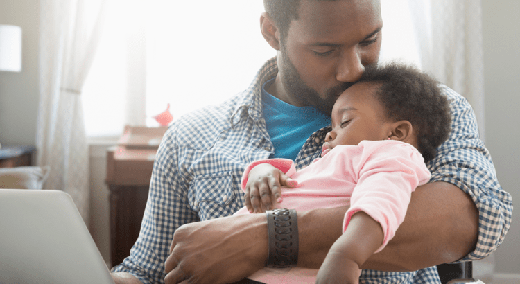 A family scene with a man holding a sleeping baby, suggesting family bonding or parenting.