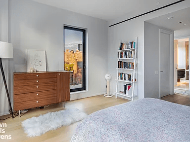 Bedroom with a wood dresser, city-view window, white bookshelf, and gray bed.