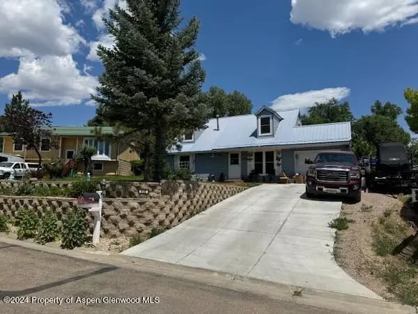 Blue house with a white metal roof, front dormer, and wide concrete driveway.