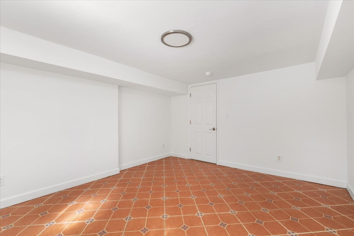 Empty room with terracotta tile flooring, white walls, and a paneled door.