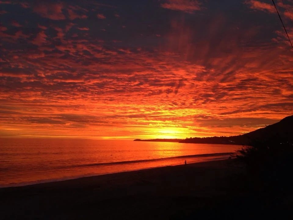Red-orange sunset over the ocean, with a dark beach and headland in silhouette.