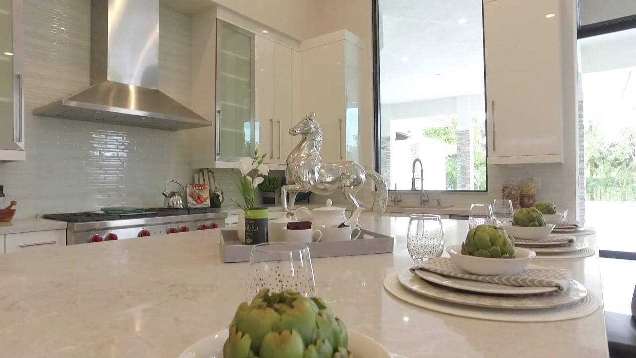 Modern white kitchen with a stone island set with artichokes and a silver horse sculpture.