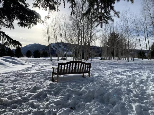 Snow-covered park with a wooden bench, bare trees, and mountains in the distance.