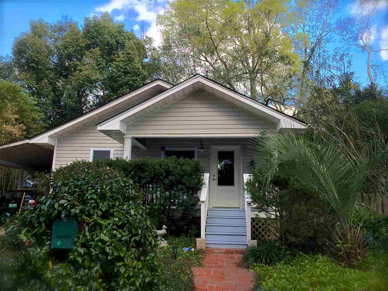 A small house with a porch stands beside a tree, creating a cozy and inviting outdoor atmosphere.
