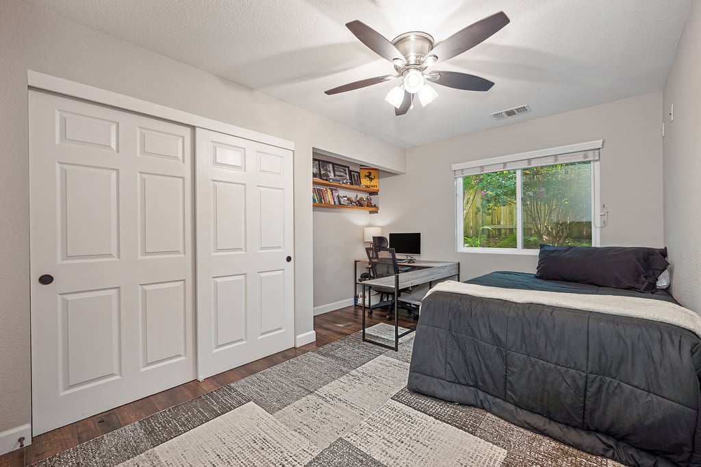 Bedroom with sliding closet doors, a desk, and a window overlooking greenery.