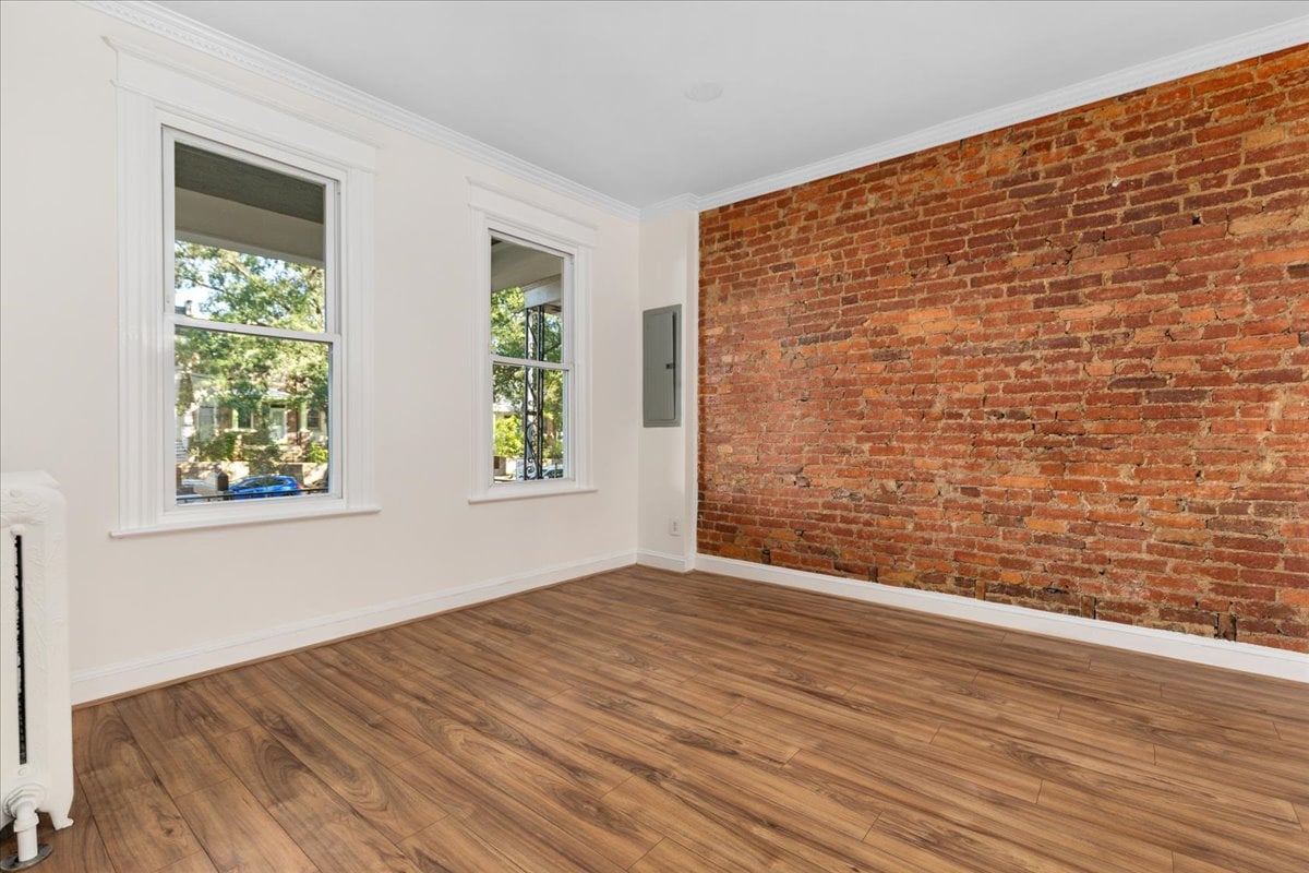 Empty room with exposed red brick wall, wood-look flooring, and two white-trimmed windows.