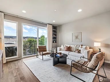 Living room with a white sofa, two brown lounge chairs, and glass doors opening to a balcony.