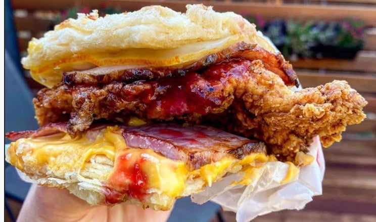 Fried chicken biscuit sandwich with melted cheese, bacon, and red sauce.