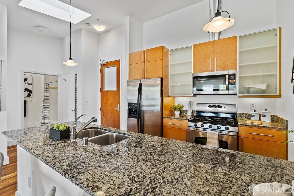 Modern kitchen with warm wood cabinets, stainless steel appliances, and a granite island with double sink.