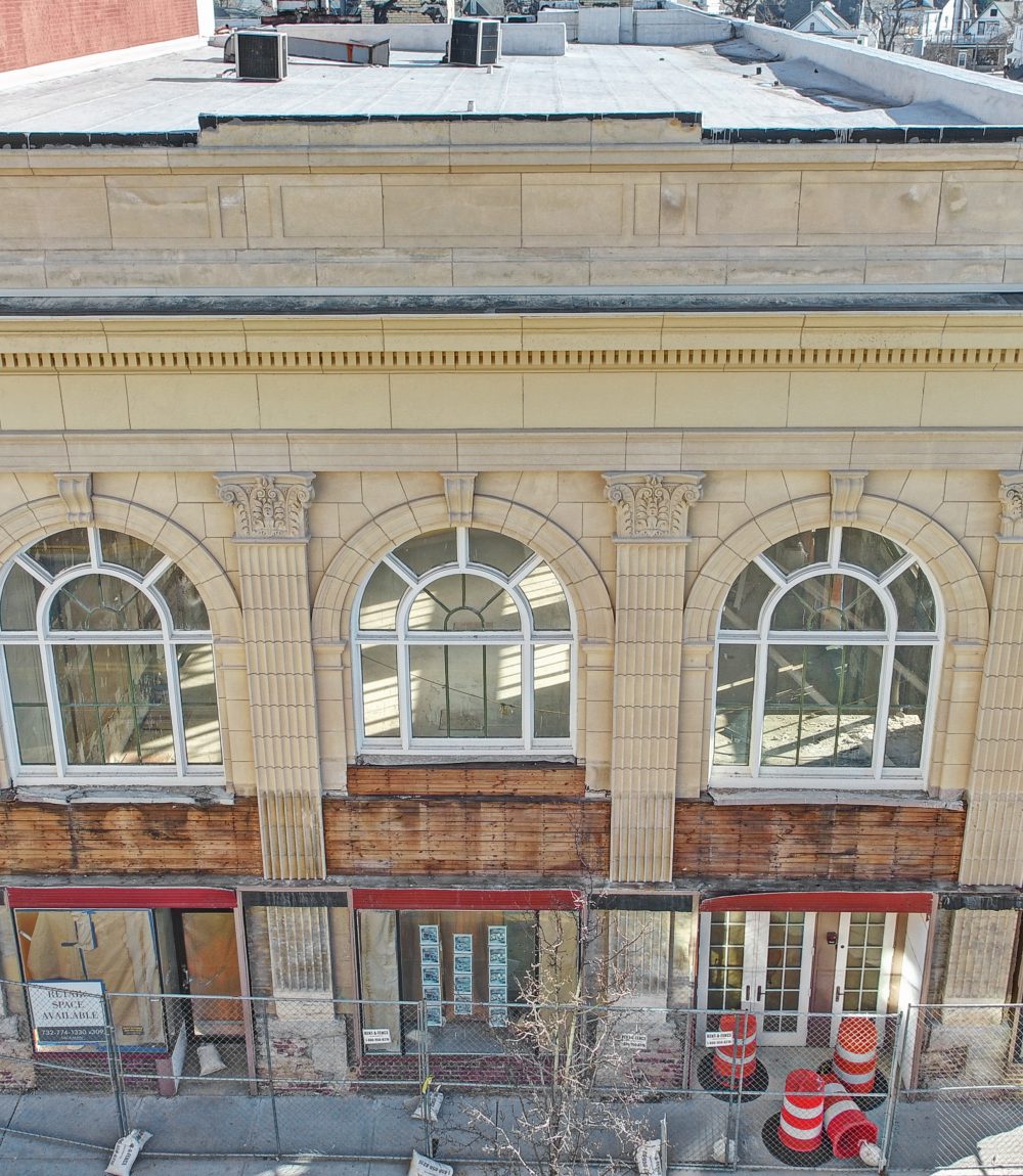 Ornate stone commercial facade with arched windows and storefronts behind construction fencing.