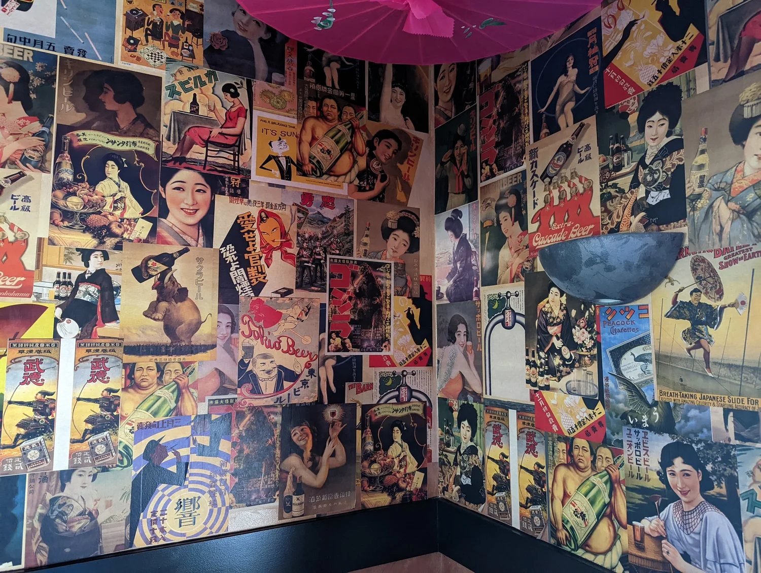 A corner of Momoku No Usagi papered floor to ceiling with vintage Japanese posters, under a pink paper umbrella.