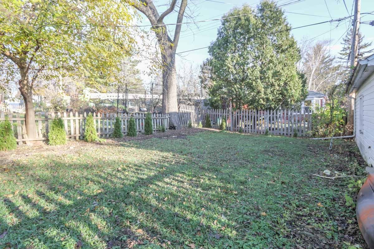 Fenced backyard with a grassy lawn, mature trees, and a wooden picket fence.