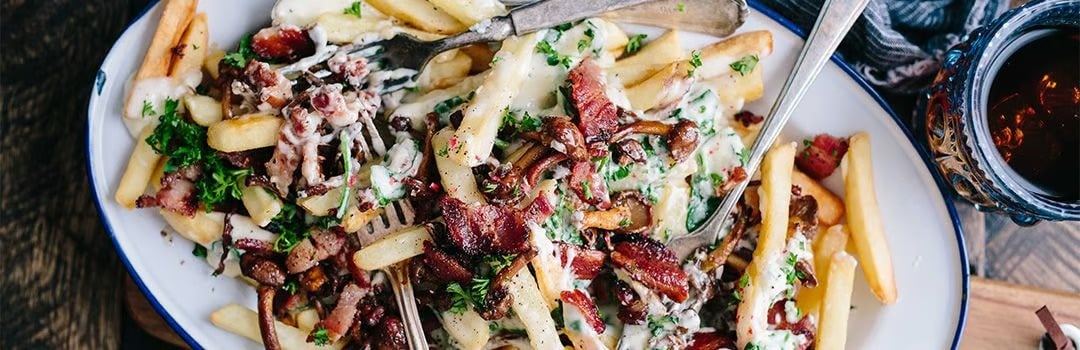Loaded fries topped with bacon, herbs, and creamy sauce, with a fork on the plate.