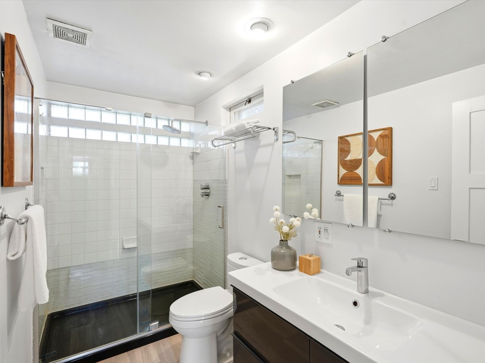 Bathroom with a glass walk-in shower, high horizontal windows and a long white vanity.