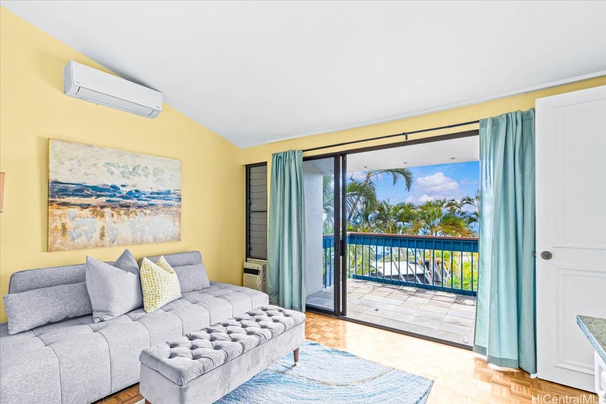 Living room with a gray sectional and sliding doors opening onto a palm-lined balcony.