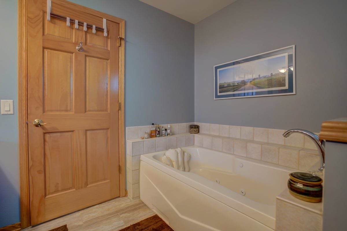 Bathroom with a large built-in tub, tiled surround, and a framed landscape print.