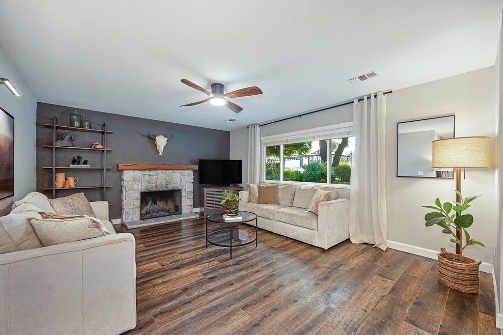 Living room with a stone fireplace, two beige sofas, and dark wood flooring.